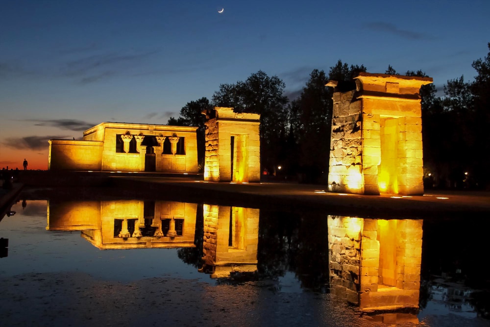 Mirador del Templo de Debod al atardecer, con su reflejo en el agua y la iluminación nocturna destacando su arquitectura egipcia.