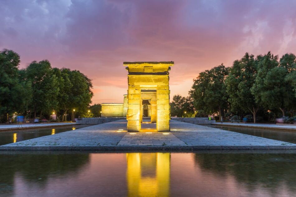 Mirador del Templo de Debod al atardecer, con colores vibrantes en el cielo y su reflejo en el agua, resaltando la arquitectura egipcia.