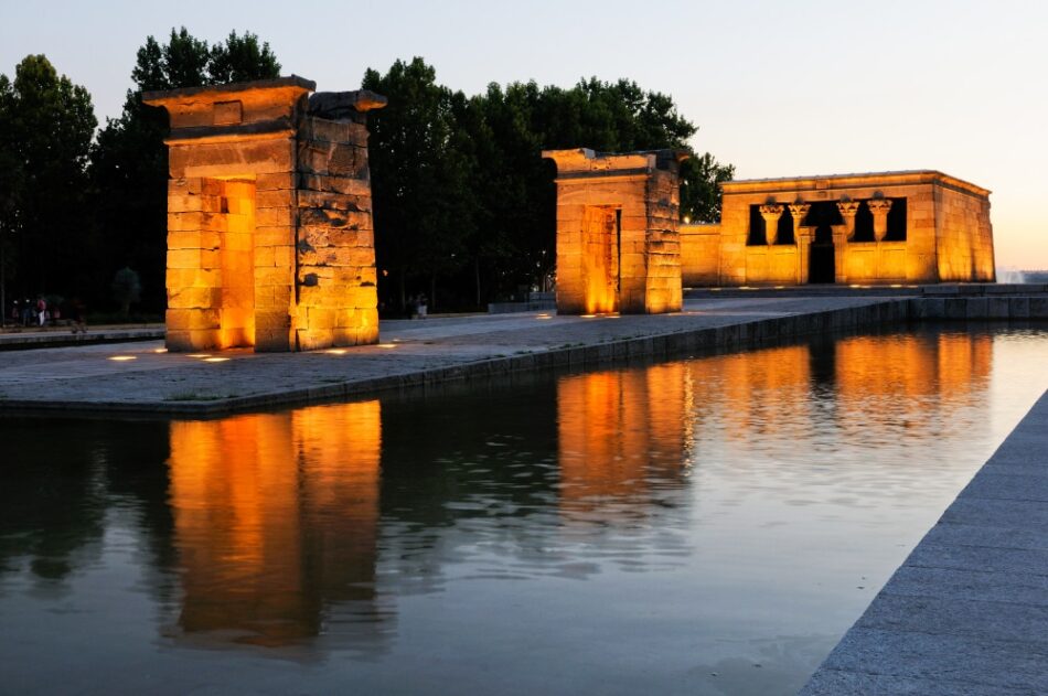 Mirador del Templo de Debod al atardecer, reflejando su majestuosa estructura en el agua, con la iluminación resaltando su arquitectura egipcia.